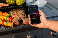 Person holding a smartphone with the Nexgrill app showing cooking temperatures and food on a barbecue with Nexgrill wireless meat probe in steak.
