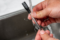Person cleaning a Nexgrill wireless meat probe under running water in a sink.